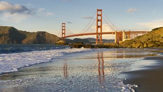 The Golden Gate Bridge in San Francisco is shown against the gray water at sunset.